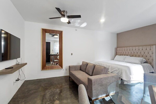 A modern hotel room with a bed, a sofa, a glass coffee table, a TV on a shelf, and a ceiling fan. - +MS +Loft Céntrico +Cómodo +Internet (Santiago de Querétaro)