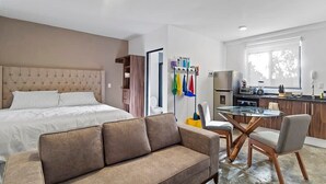 A modern hotel room with a bed, a sofa, a glass dining table, and a kitchen area. - +MS +Loft Céntrico +Cómodo +Internet (Santiago de Querétaro)