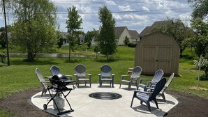 Eine Außenpatio-Terrasse mit Adirondack-Stühlen, einem Grill und einer Feuerstelle.