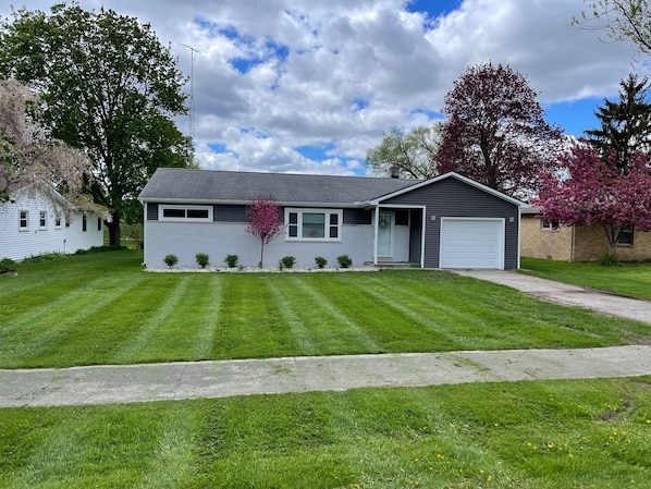 A single-story house with a garage, a well-maintained lawn, and mature trees.