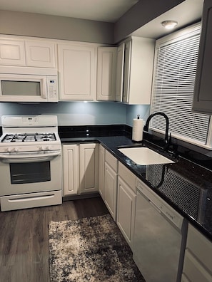 A kitchen with white cabinets, a stove, a microwave, a sink, and a dishwasher.