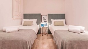 Ein Hotelzimmer mit zwei Betten, beide mit grauem Kopfteil und weißer Bettwäsche. Dazwischen steht ein kleiner Tisch mit Pflegeartikeln.