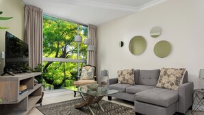Ein modernes Wohnzimmer mit einem Glastisch, einem grauen Sofa und einem Fernseher auf einem Holzständer.