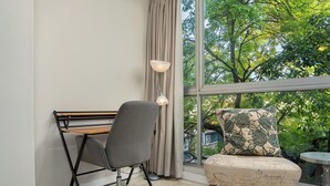 Ein modernes Zimmer mit Schreibtisch, Stuhl und Blick auf Bäume durch ein großes Fenster.