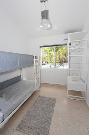 A bunk bed with a grey mattress, a white shelving unit, and a window with a view of palm trees. - Villa Paradis with a private pool, palapa, tropical garden, and complete privacy (Grote Berg)