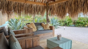 Un espace extérieur abrité, doté de mobilier en bois et d’un toit de chaume.