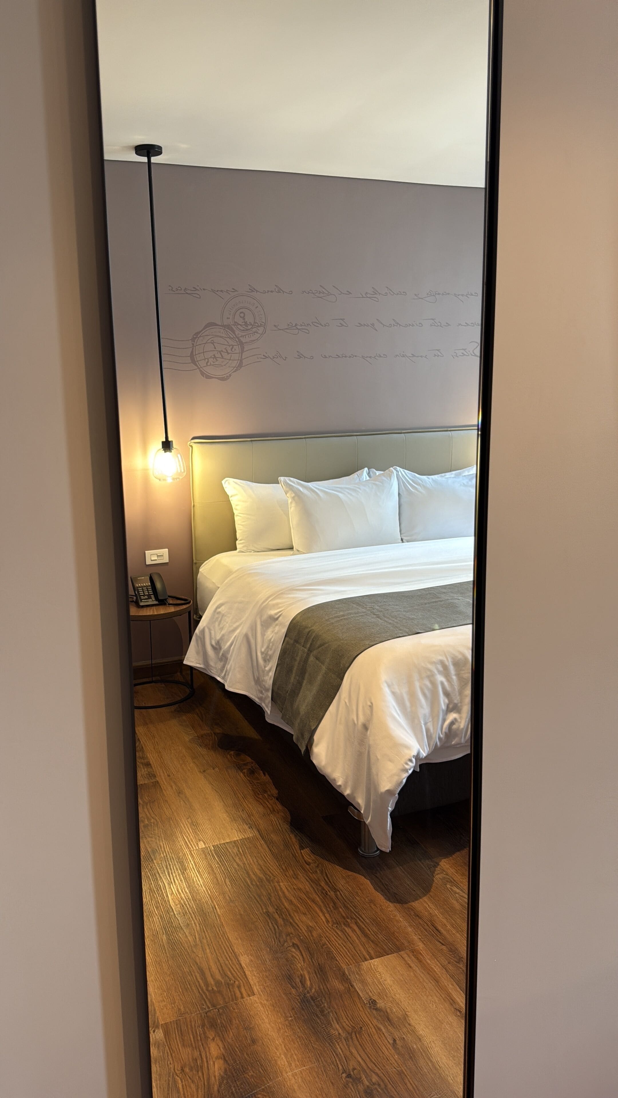 Una habitación de hotel con cama, mesita de noche, lámpara y un elemento decorativo en la pared.