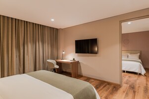 Una habitación de hotel con cama, escritorio, silla, televisor y espejo.