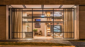 A modern building entrance with glass doors, a visible interior with bookshelves and seating, and a well-maintained lawn area.