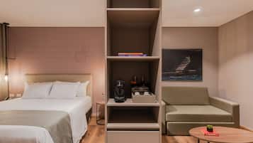 A hotel room with a bed, a sofa, a coffee table, a bookshelf, and a painting on the wall.