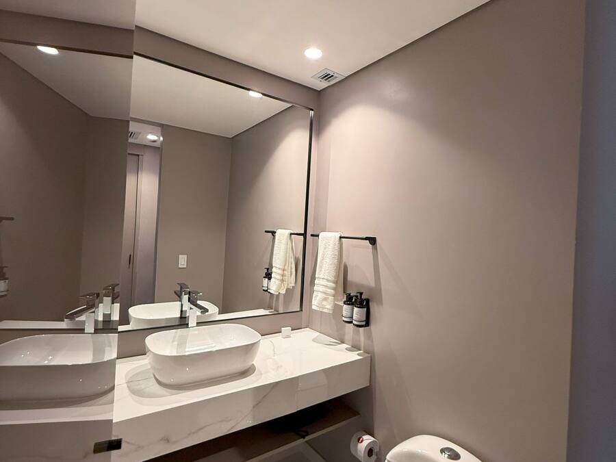 A modern bathroom with a large mirror, two sinks, and a toilet.