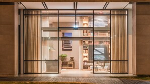 A hotel entrance with a modern design, large glass doors, and a visible interior with bookshelves and a staircase.