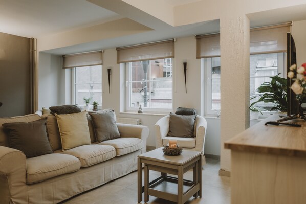Un salon moderne avec un canapé beige, une petite table sur laquelle est posée une bougie et une table d’appoint en bois.
