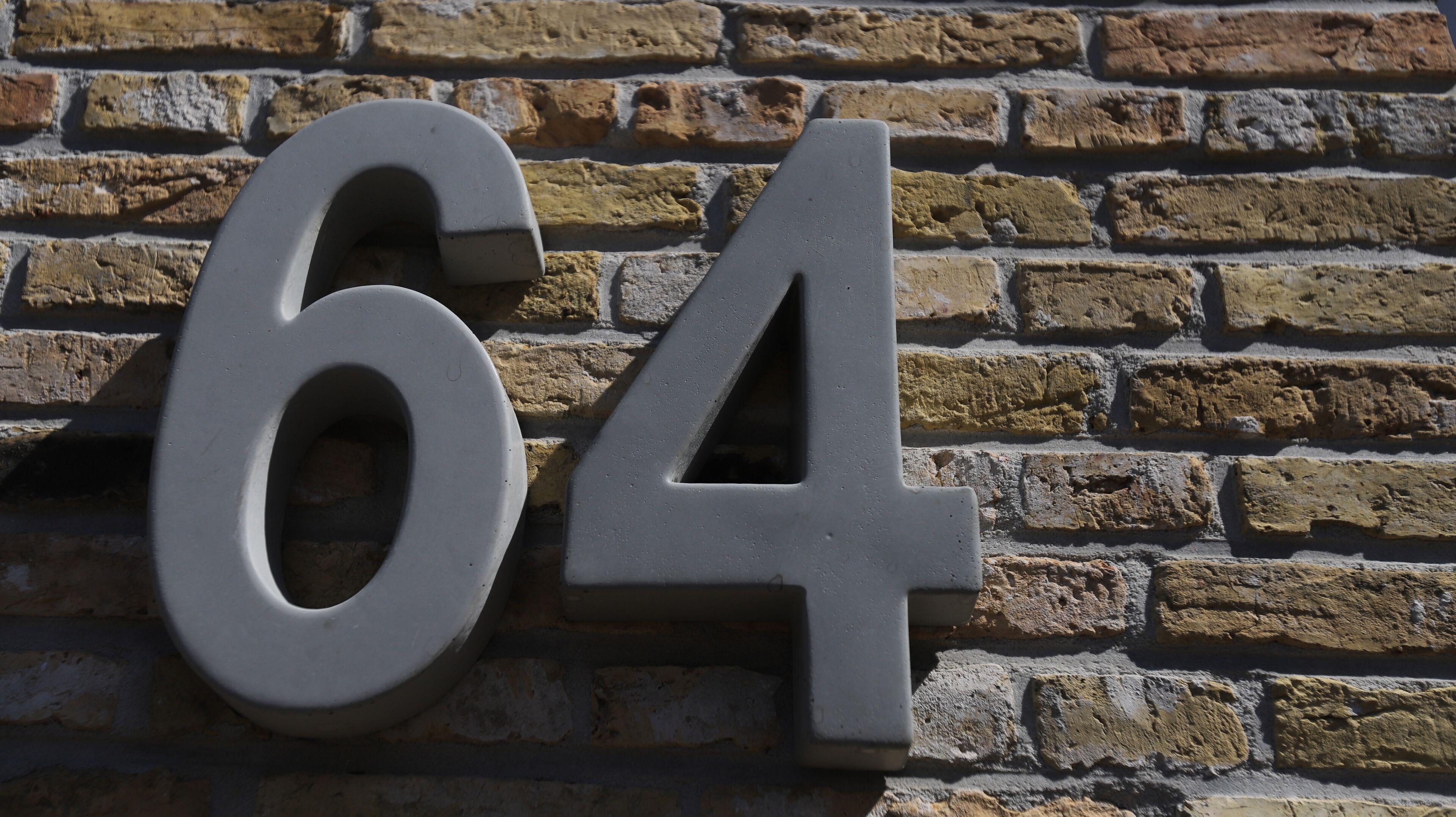 Un grand chiffre « 64 », en relief, fixé sur un mur de briques.