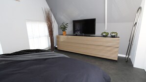 Et moderne soveværelse med en seng, en trækommode, et fjernsyn og et vindue med persienner.