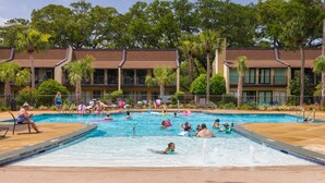 Un espace piscine comprenant plusieurs bassins, des chaises longues et un panneau indiquant la présence d’un sauveteur.