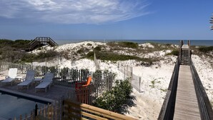 A beachside resort with a wooden boardwalk leading to a sandy beach, a pool area with lounge chairs, and a clear view of the ocean.