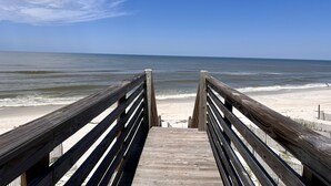 A wooden boardwalk leading to a beach with a clear sky.