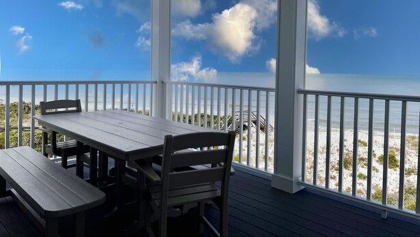 A covered outdoor area with a table and benches, overlooking a beach with a pier.
