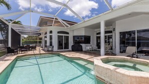 Ein Poolbereich mit überdachter Terrasse, Sitzgelegenheiten im Freien und einer Grillmöglichkeit.