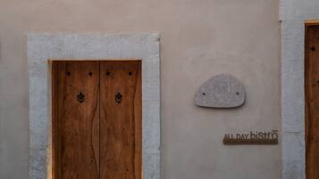 Una porta de fusta amb una placa de pedra i un rètol que indica 'ALLDAY bistro' amb l'horari d'obertura.