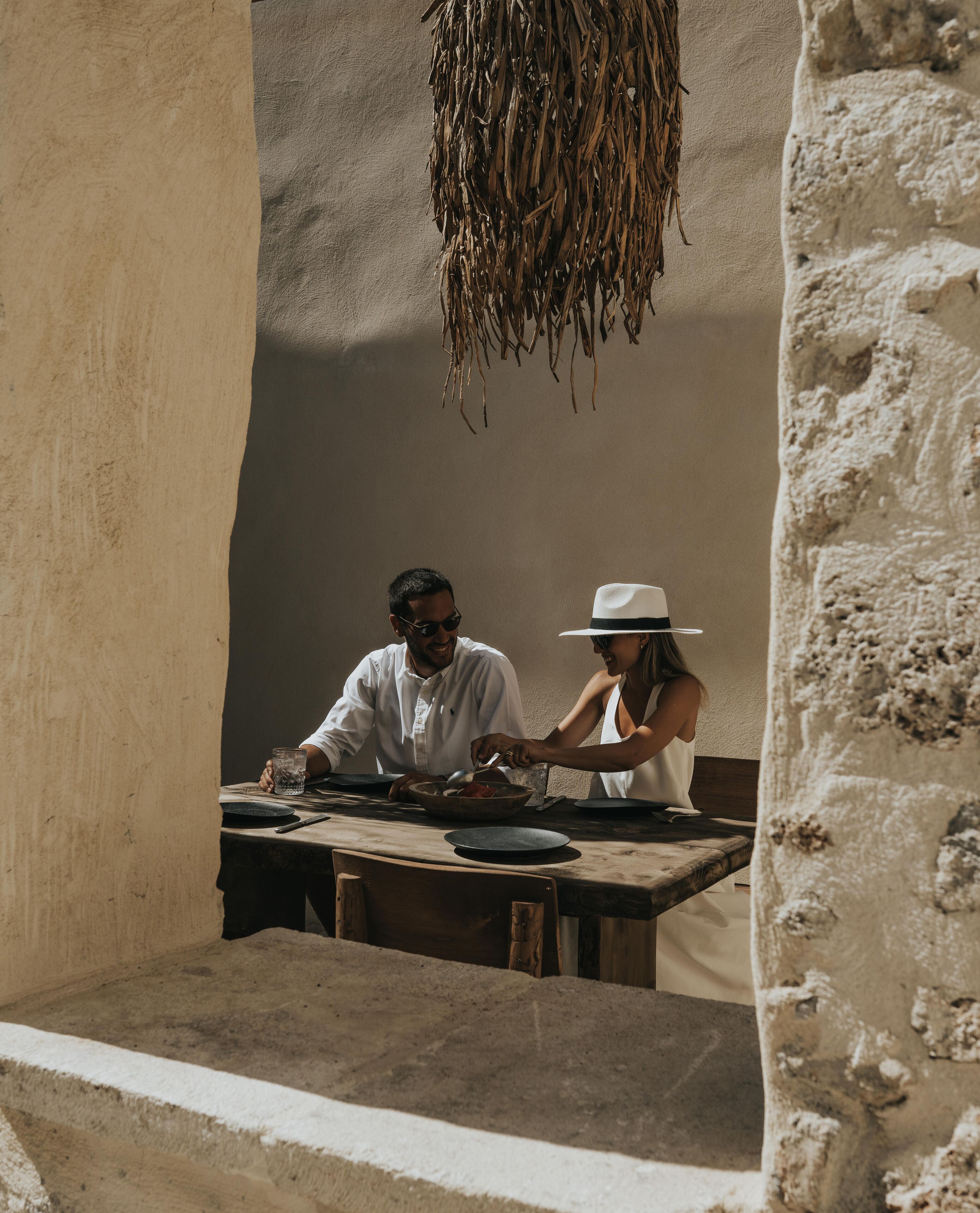 A couple dining at a table with a rustic setting, including a hanging plant and a textured wall.