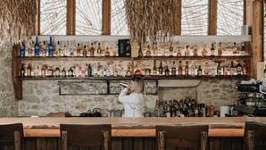 A bar with wooden shelves stocked with various bottles, a bartender, and rustic decor. - Manili Suites & Villas, an SLH Hotel (Archanes-Asterousia)