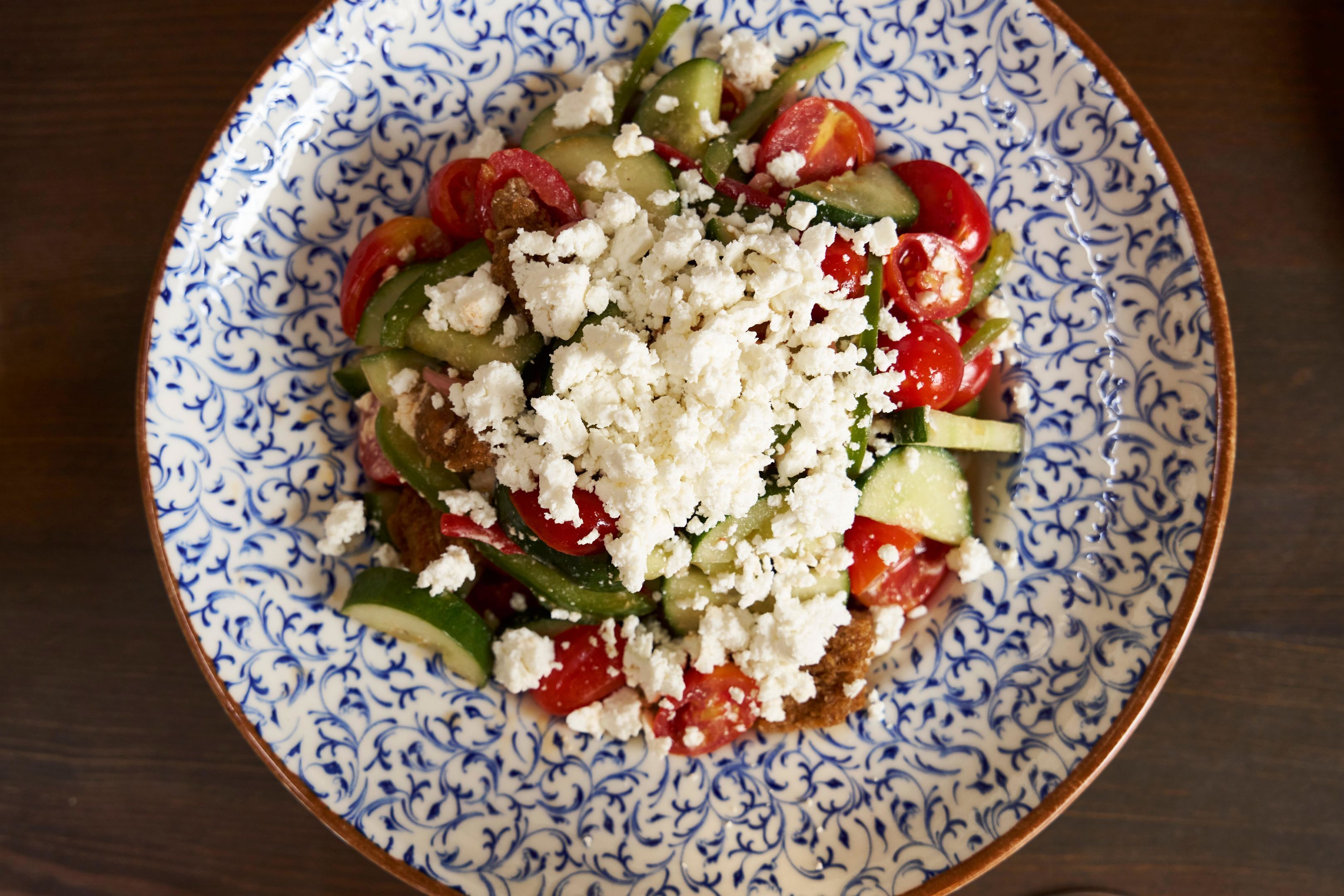 En tallrik med sallad, fetaost, tomater, gurka och gröna paprikor.