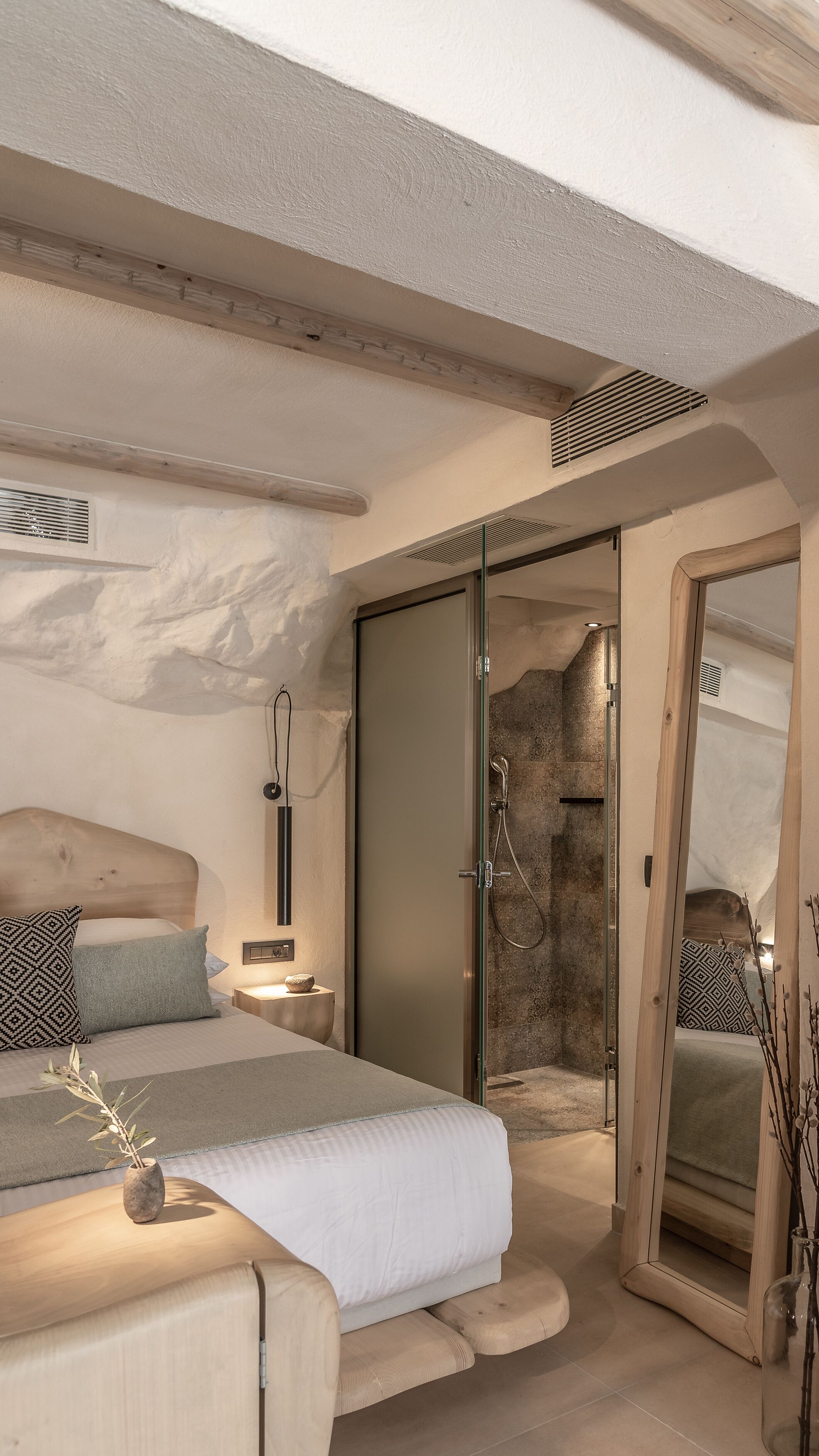 A modern bedroom with a large bed, a walk-in closet, and a stone shower area.