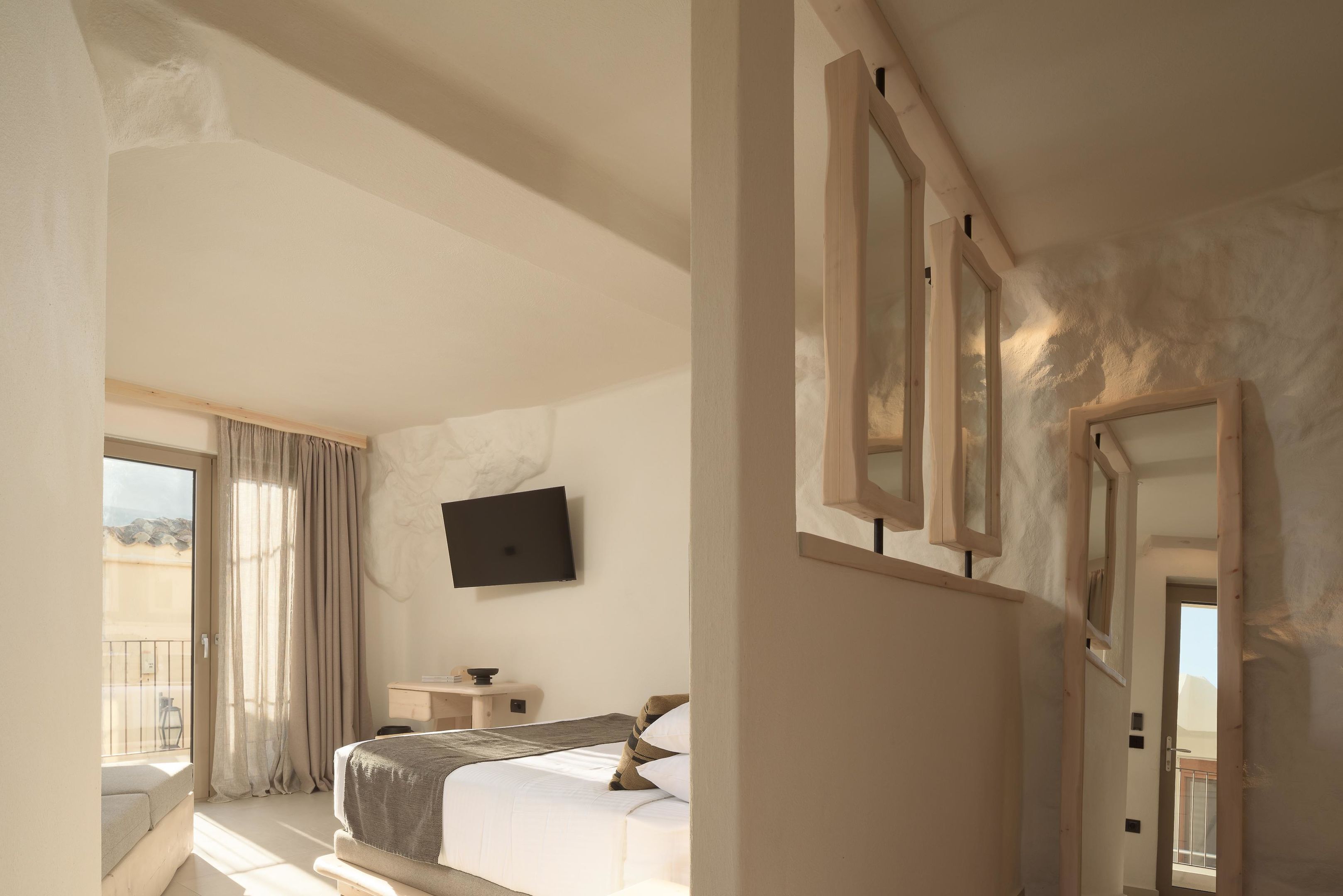 A hotel room with a bed, a TV, a small bedside table, and a window with curtains.