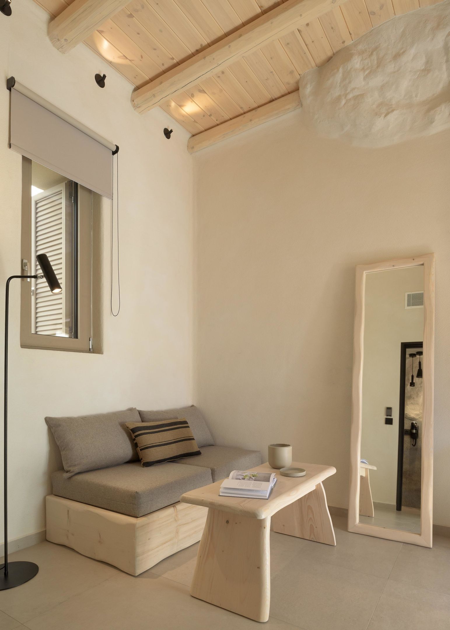 A minimalist living room with a sofa, a small wooden table, a floor lamp, and a mirror.