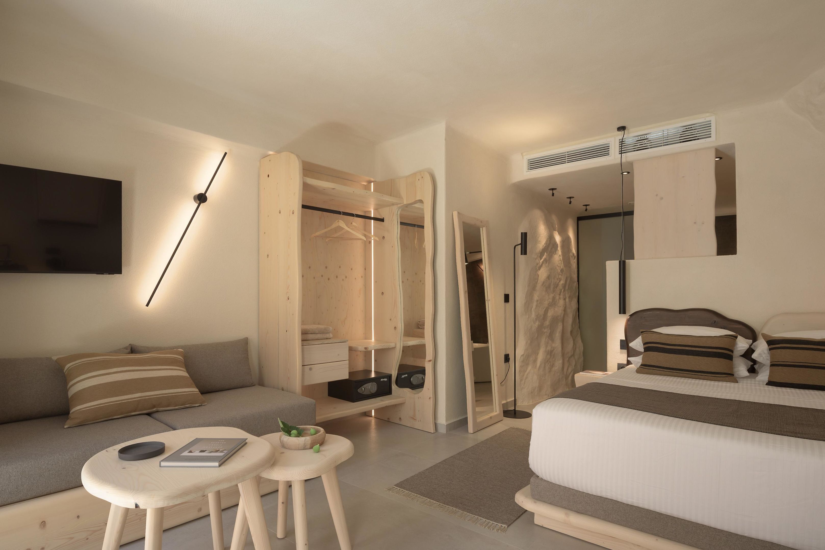 A modern hotel room with a sofa, a small table, a bed, a walk-in closet, and a large mirror.
