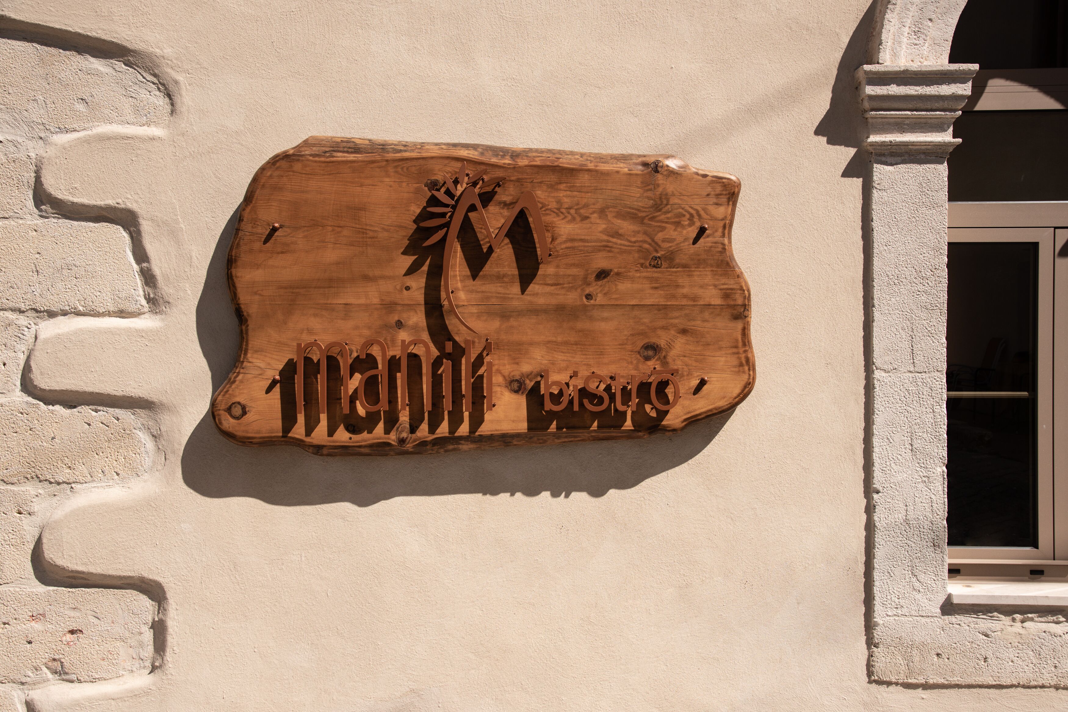 Ein hölzernes Schild mit einem eingravierten Palmenbaum und Schriftzug an einer Gebäudefassade.