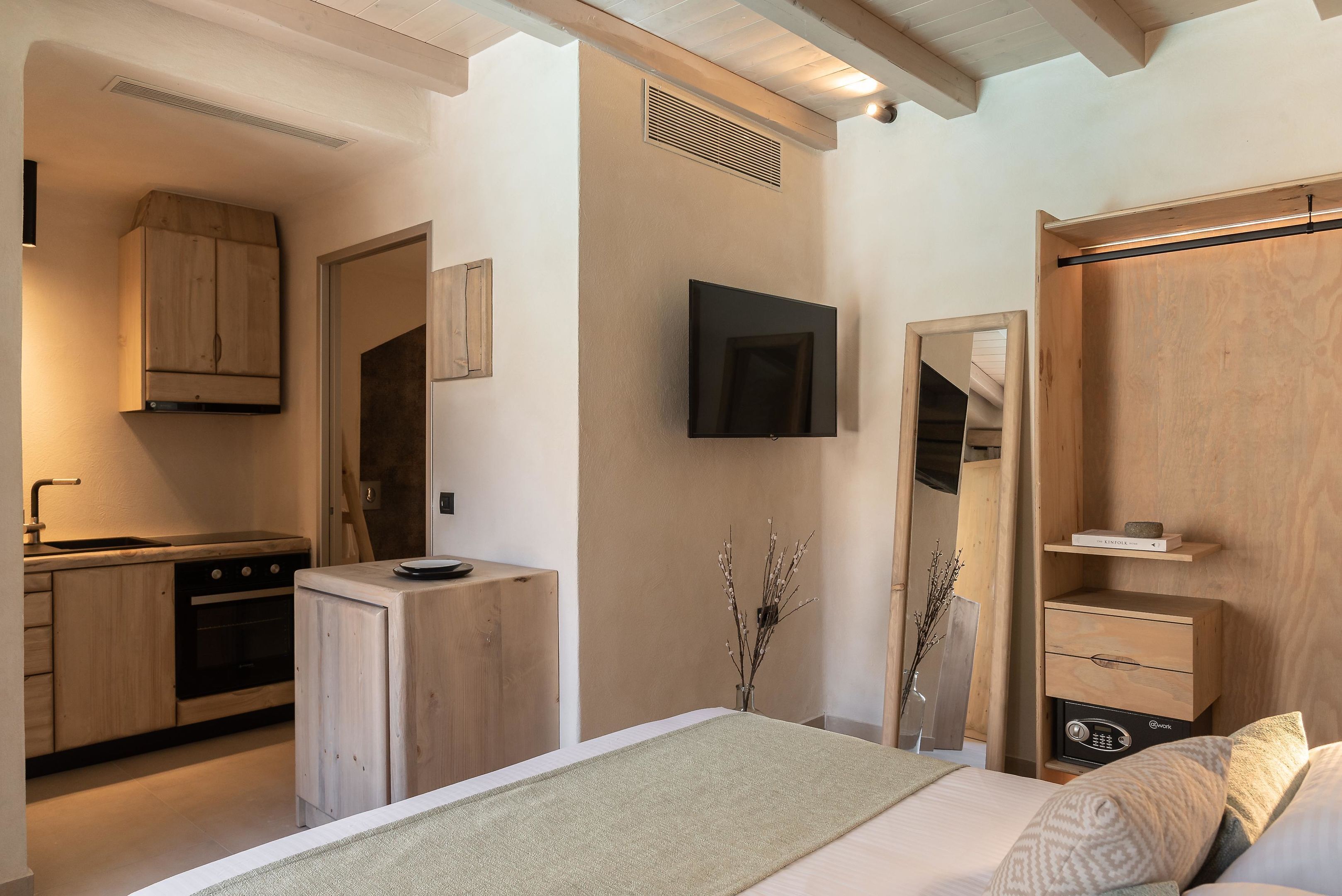 Un dormitorio moderno con cama, mesita de noche y armario. Se ve una cocina al fondo con estufa y armarios.