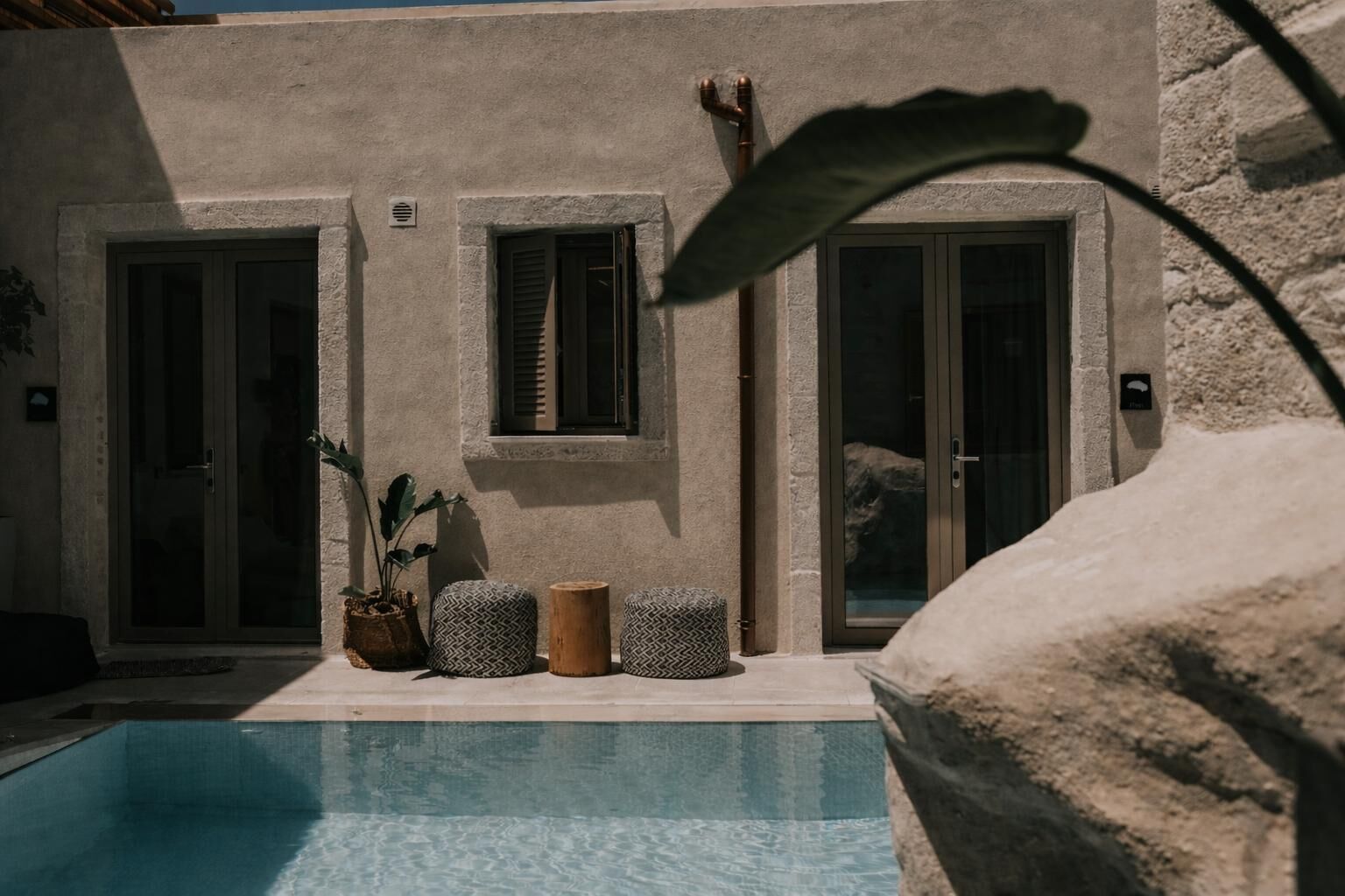 Un'area a bordo piscina con un muro in pietra, due porte e una finestra con persiane.