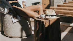 A person sitting on a bean bag chair with a wooden table beside them, a cup, and a straw hat on the table. - Manili Suites & Villas, an SLH Hotel (Archanes-Asterousia)