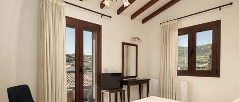 A bedroom with a bed, a chair, a desk, a mirror, and a view of the outdoors.