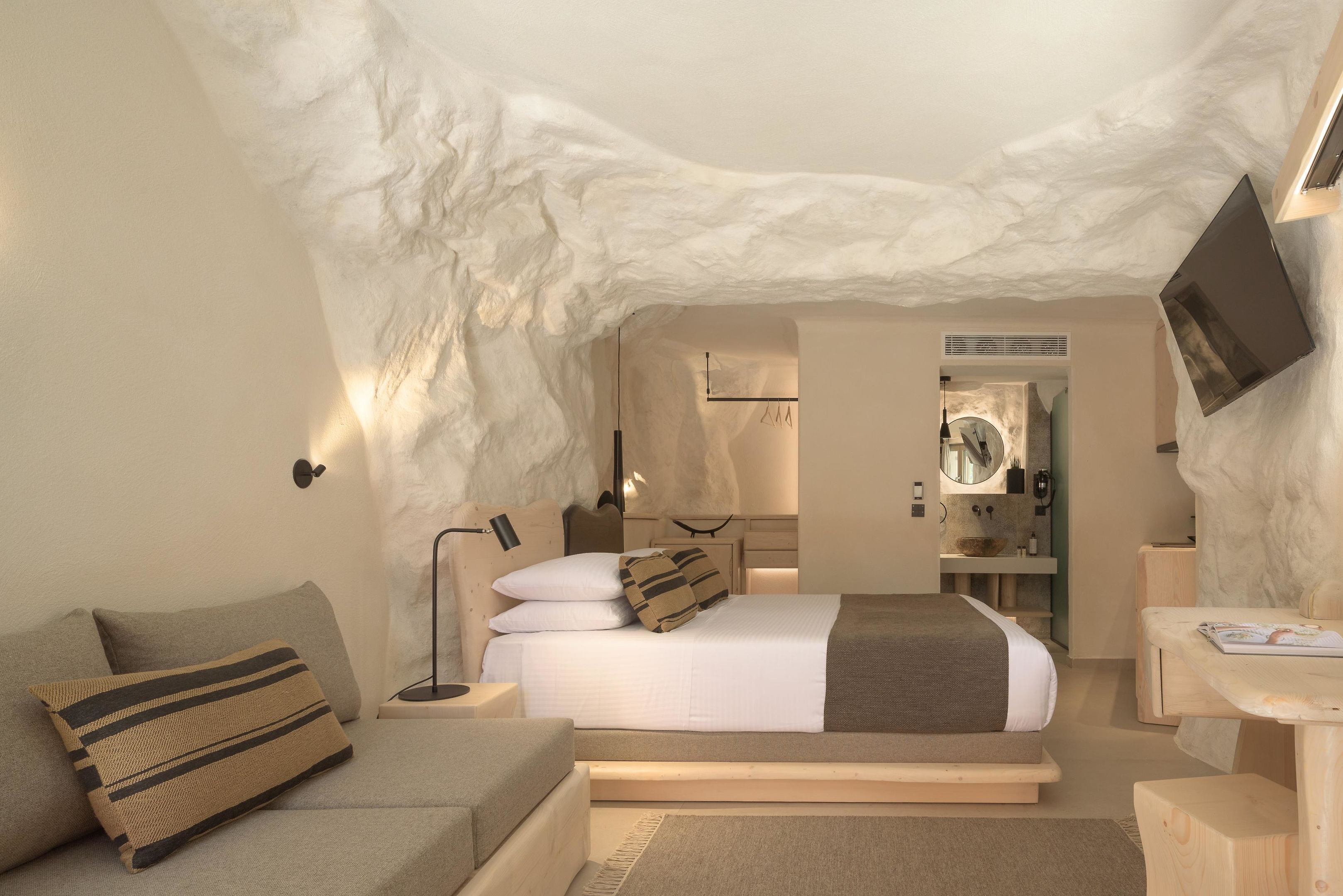 A modern bedroom with a unique ice cave ceiling, a bed with a white and brown bedspread, a bedside table with a lamp, and a wooden nightstand.