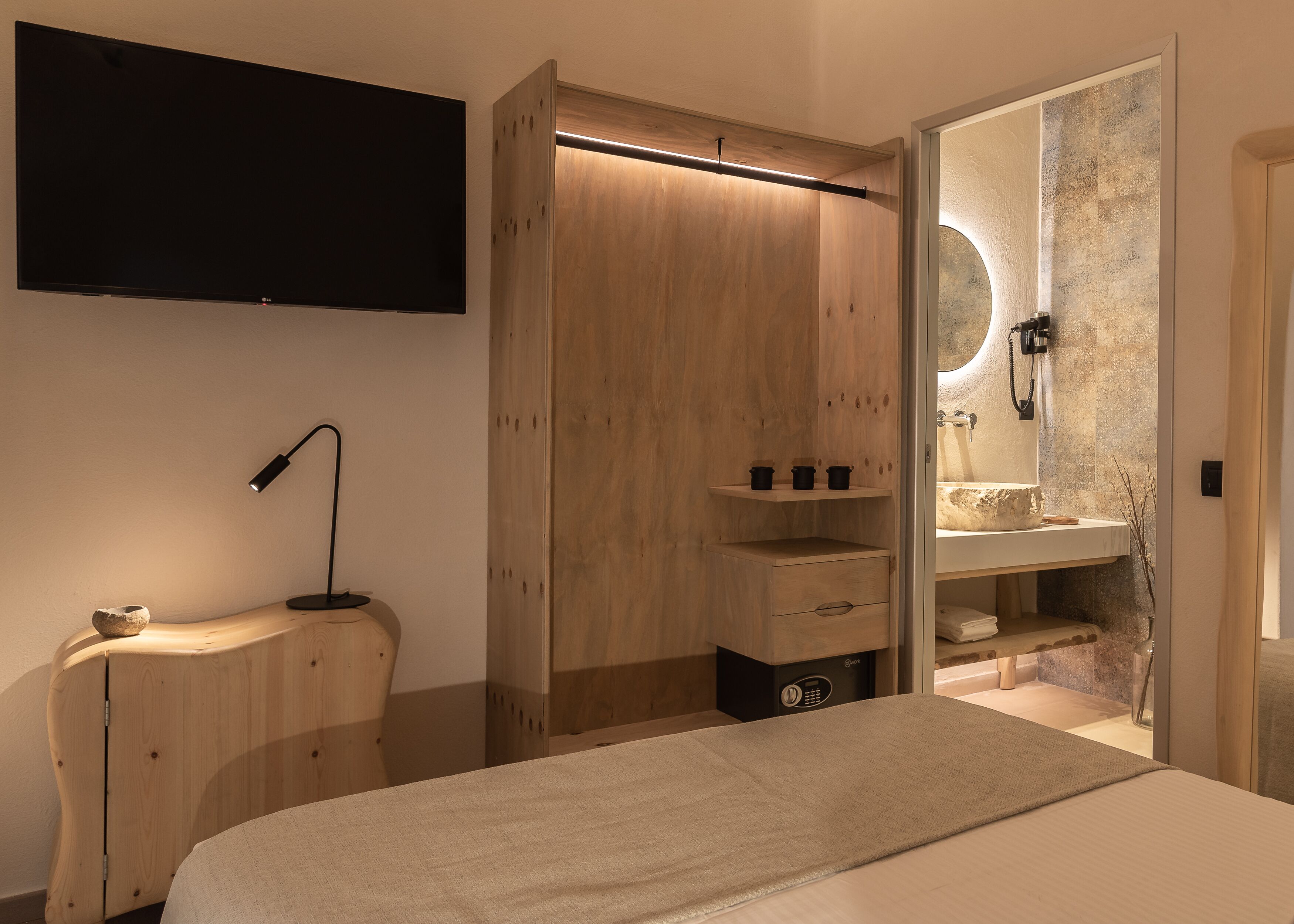 Una camera da letto moderna con un letto, una TV, un armadio in legno, una toeletta con specchio e un piccolo ripiano con articoli da toilette.