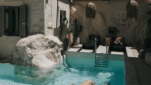 A swimming pool with a person swimming, a stone wall, and a wooden pergola. - Manili Suites & Villas, an SLH Hotel (Archanes-Asterousia)