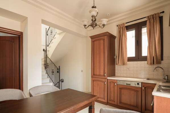 A kitchen with wooden cabinets, a dining table, and a staircase leading to another level.