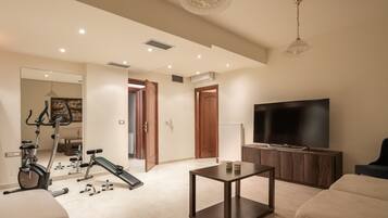 A modern living room with a flat-screen TV, a sofa, a coffee table, and exercise equipment.