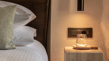 Una cama bien hecha con almohadas, una mesita de noche con un vaso de agua y una lámpara de pared.