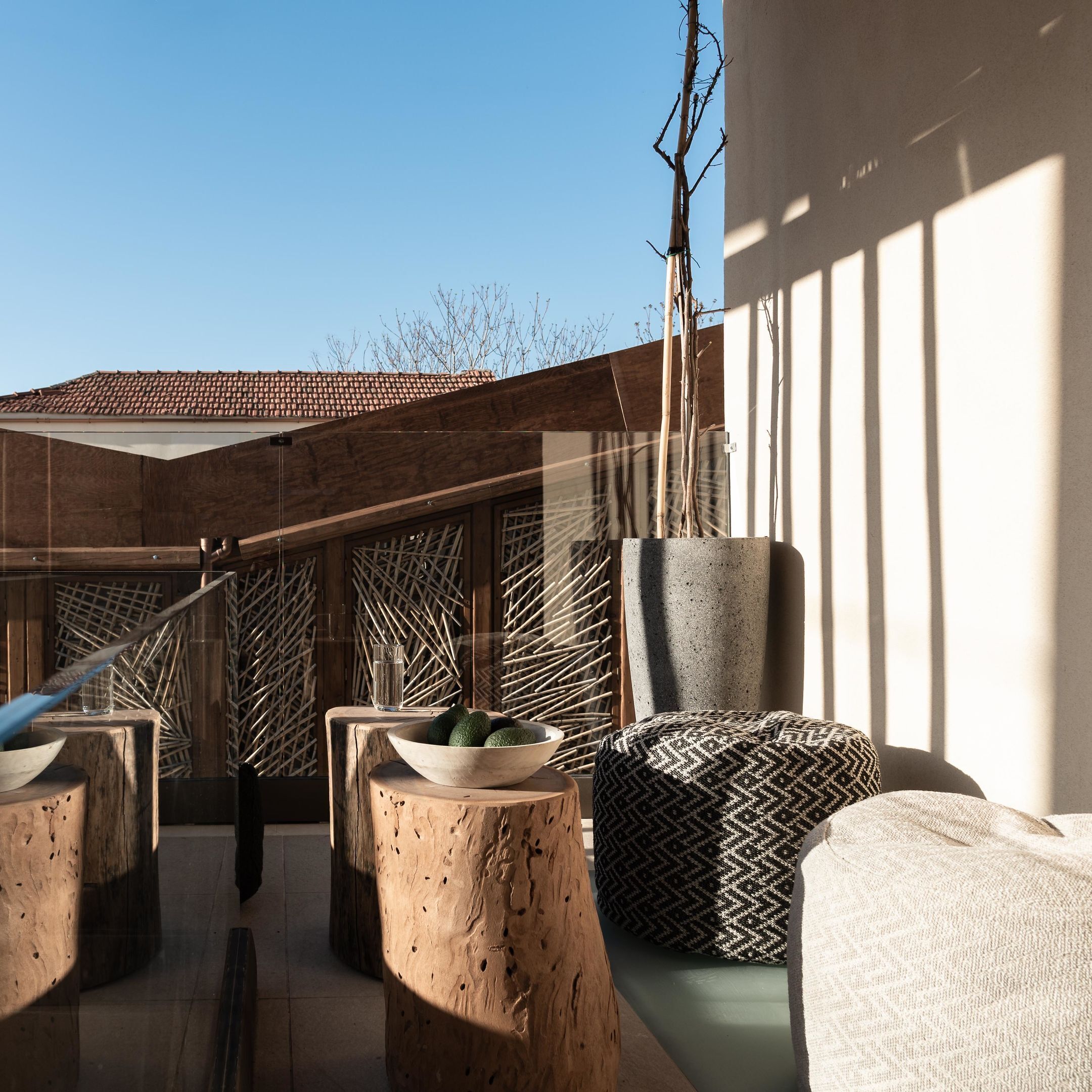 Un espacio al aire libre con taburetes de madera, un muro tejido y una jardinera de hormigón.