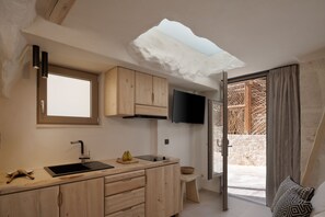 A modern kitchen with wooden cabinets, a black countertop, a built-in sink, and a flat-screen TV mounted above it. - Manili Suites & Villas, an SLH Hotel (Archanes-Asterousia)
