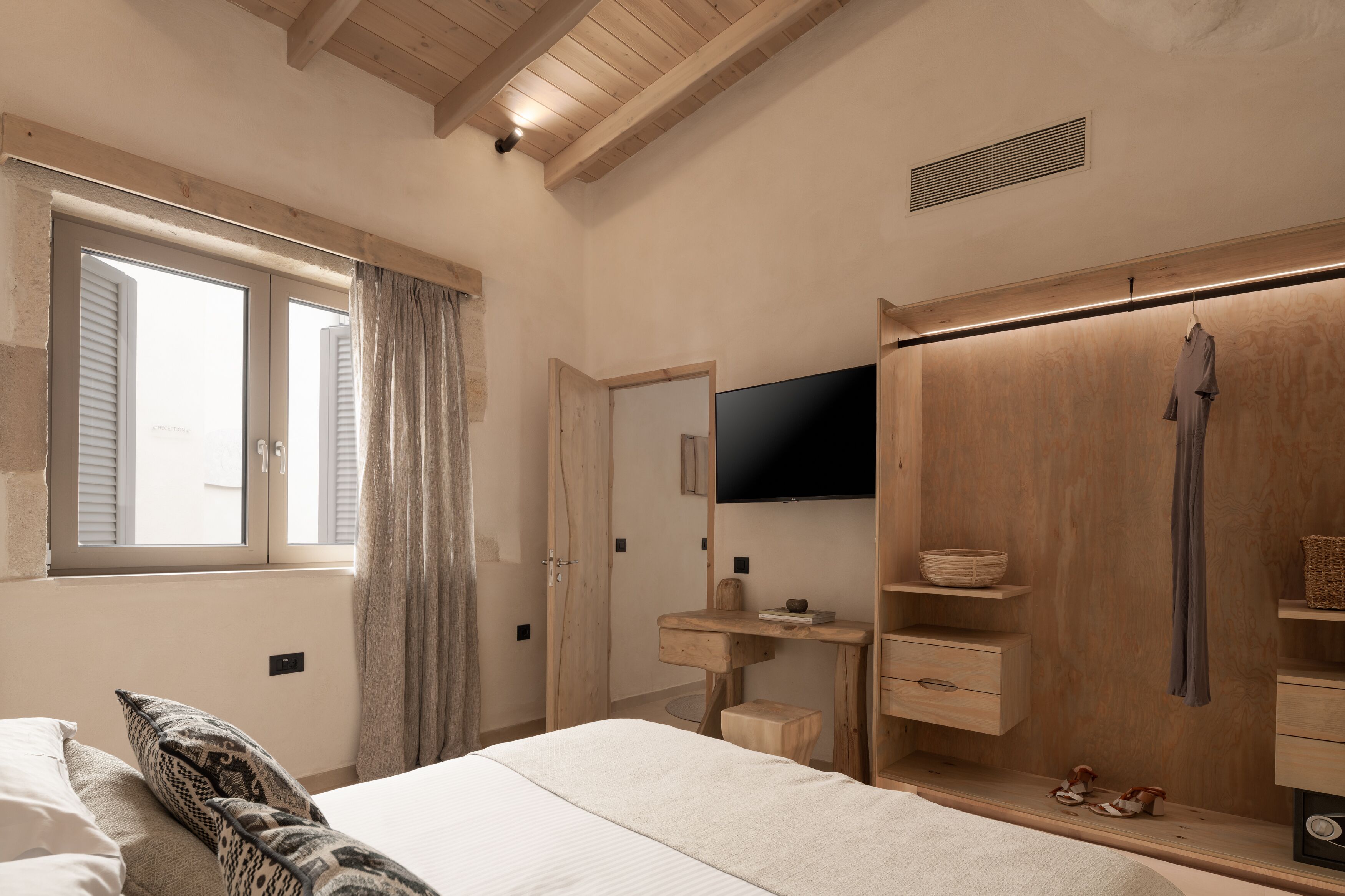 A bedroom with a bed, a wooden wardrobe, a television, and a window with curtains.