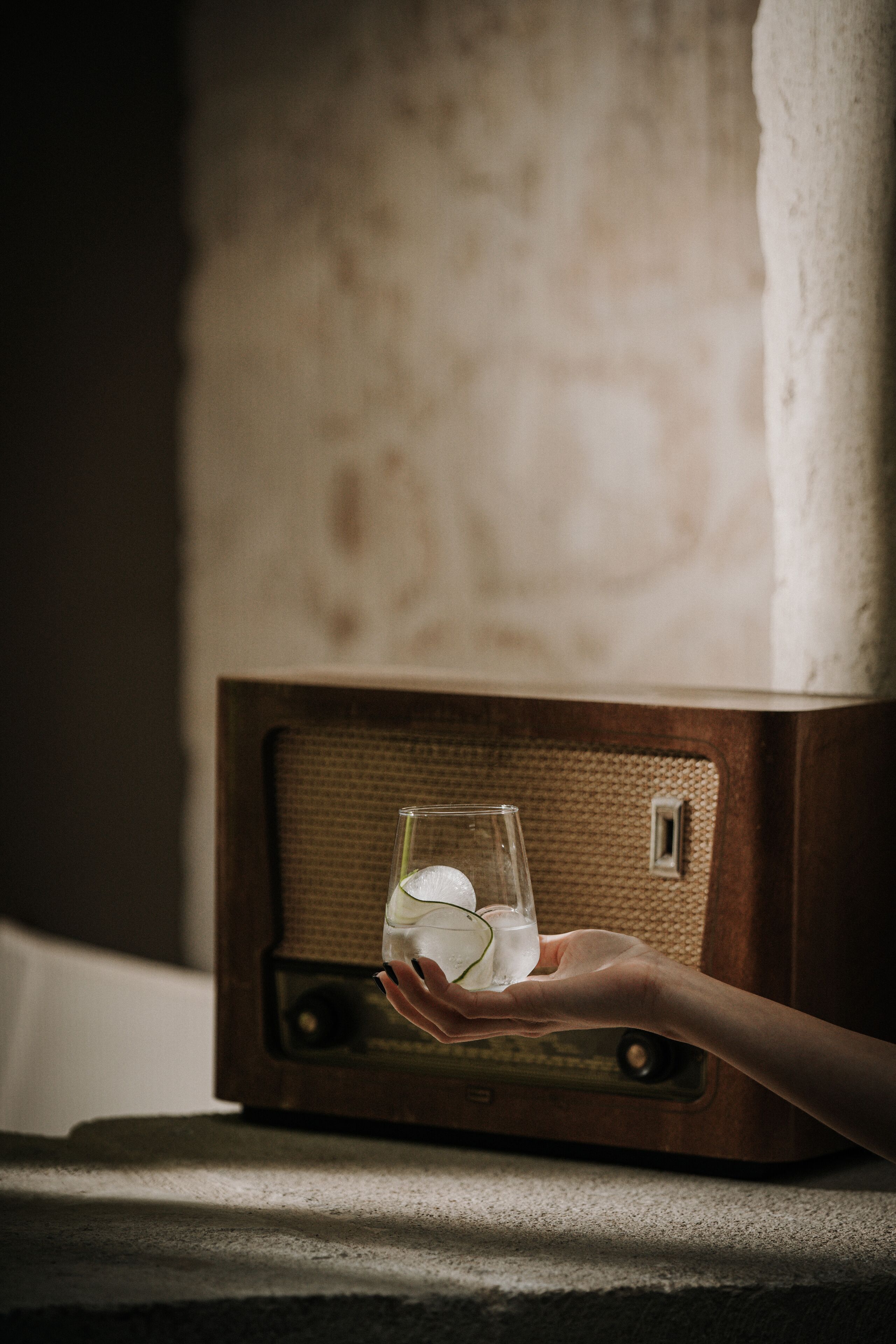 A hand holding a glass with ice cubes near a vintage radio.