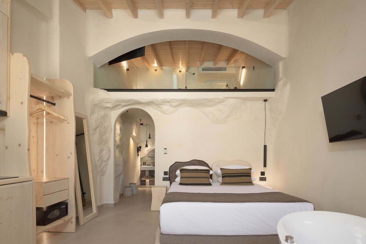 A bedroom with a bed, a vanity, and a television on the wall.