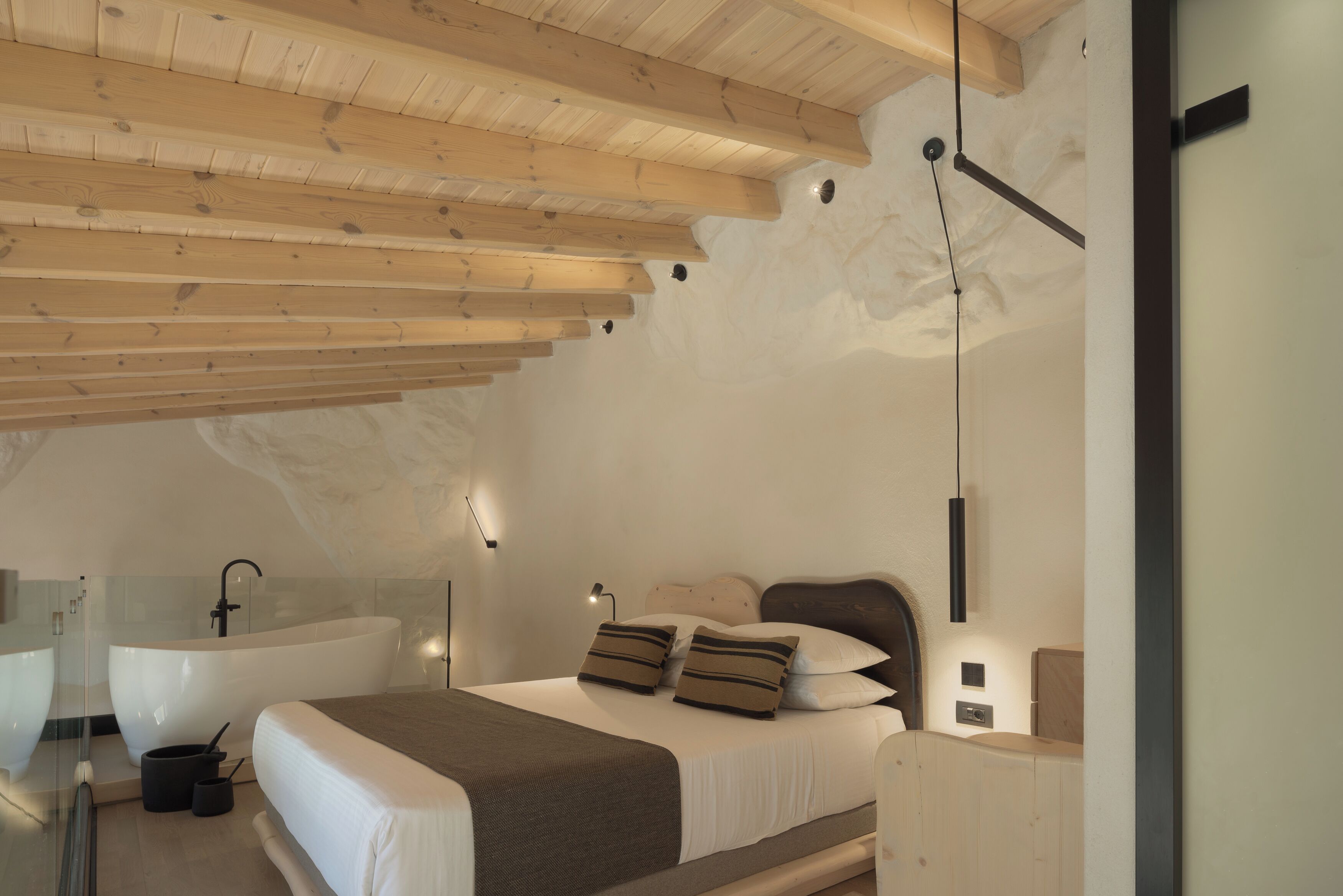 Un dormitorio moderno con una cama grande, una bañera integrada y un techo de madera.