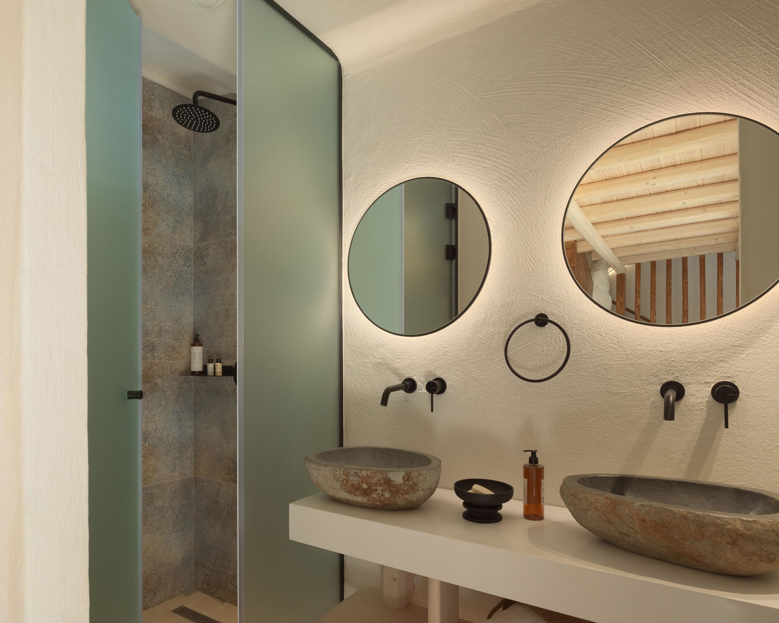 Ein modernes Badezimmer mit einem großen Spiegel, zwei steinernen Waschbecken und einer Duschkabine.